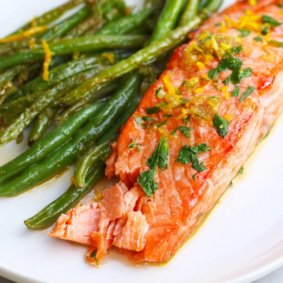 Crispy roasted green beans and tender flaky salmon fillets on a sheet pan, glistening with lemon garlic herb marinade.  