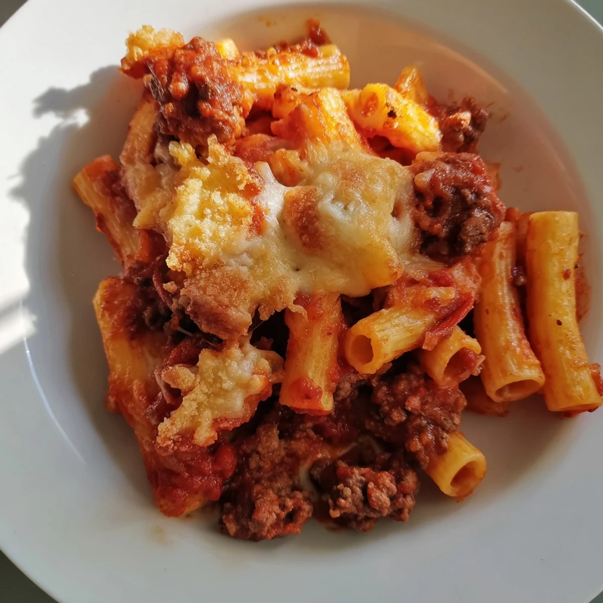 Homemade baked ziti with ground beef, topped with melted mozzarella and served alongside a fresh green salad.