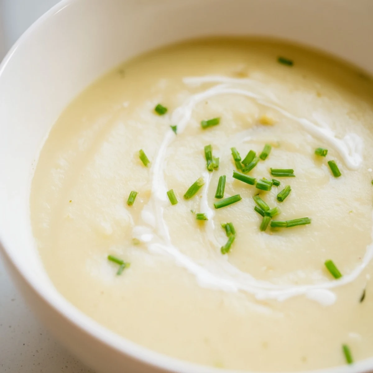 Rustic white bread slices dip into a bowl of creamy potato leek soup, garnished with fresh chives and a swirl of cream.