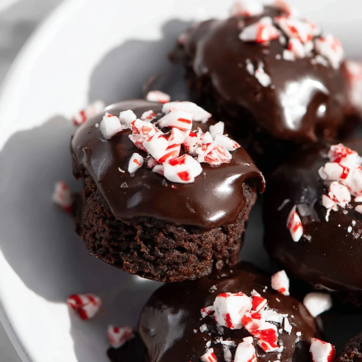 Four fudgy Mint Brownie Bites with shiny ganache and crushed peppermint on a white plate.