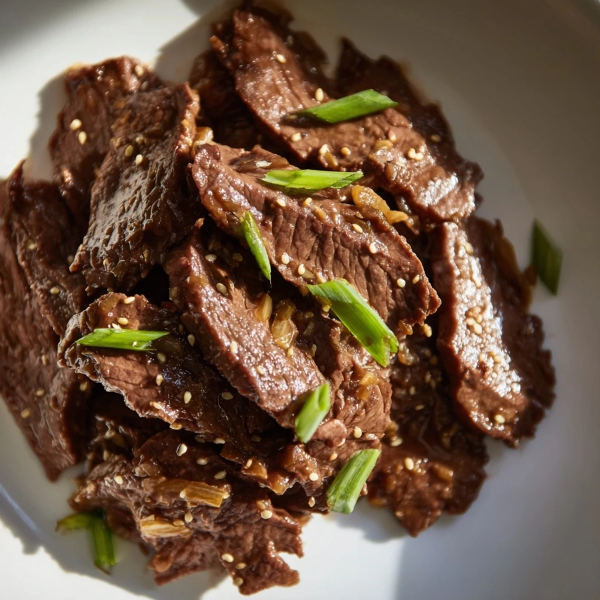 Golden-brown slices of beef in a glossy sauce, garnished with green onions and sesame seeds for Ultimate Slow Cooker Mongolian Beef.