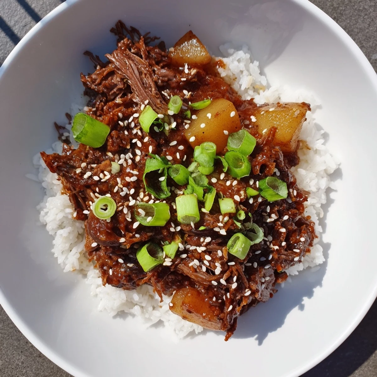 Close-up of tender shredded Crock Pot Korean Beef simmering in a glossy, savory-sweet sauce, garnished with green onions and sesame seeds.