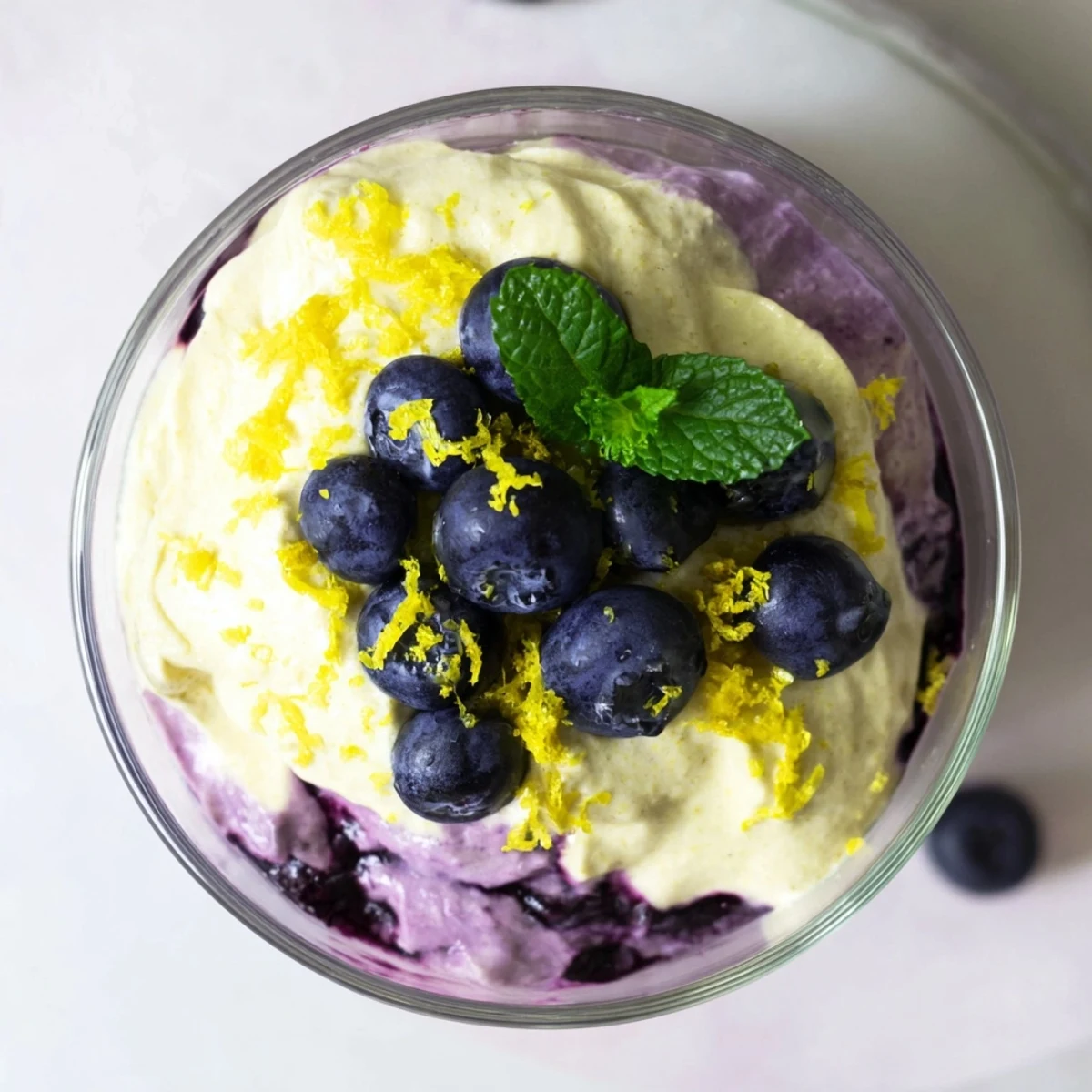 Elegant Lemon Blueberry Mousse served in a clear glass, revealing swirls of yellow and purple with a mint leaf topping.