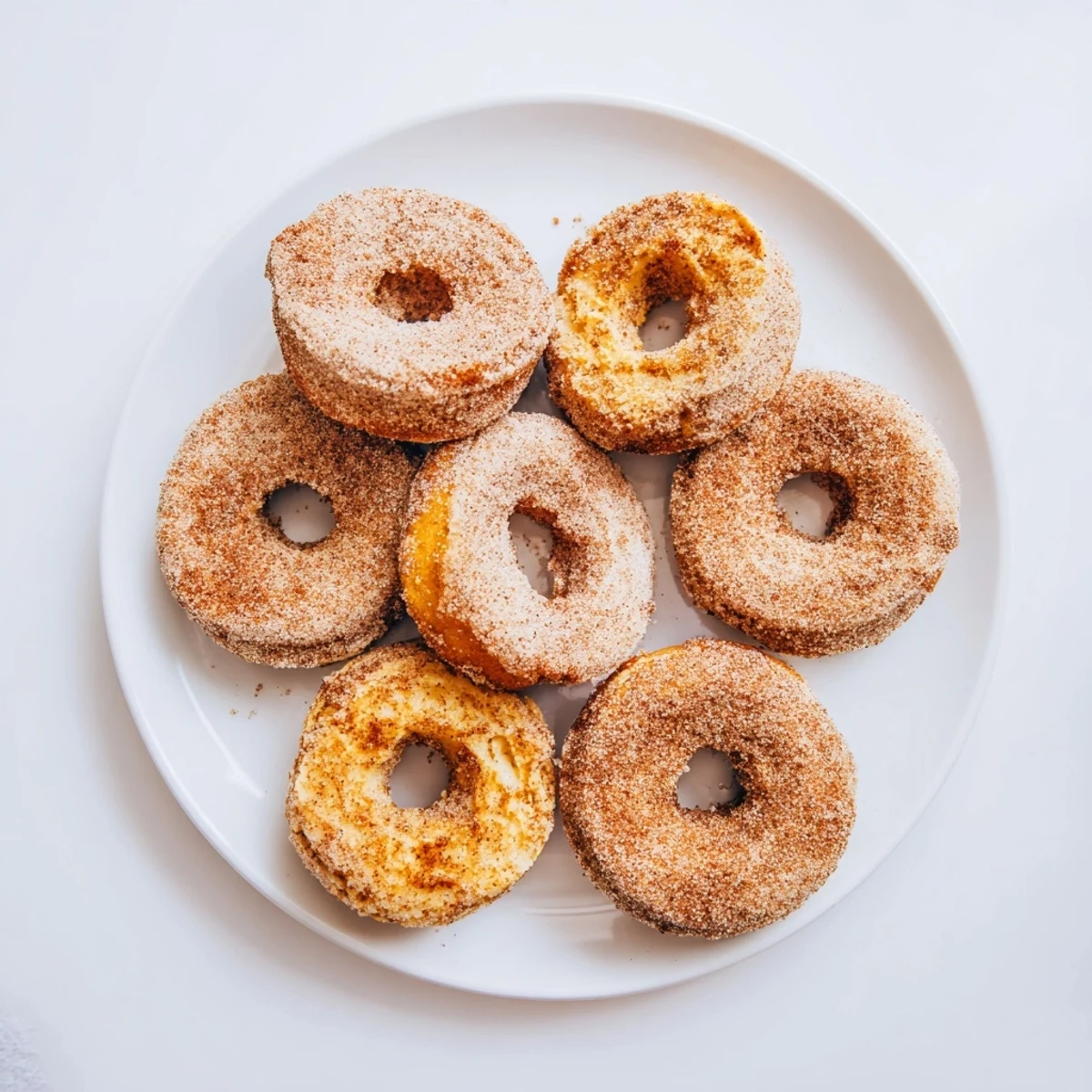 A hand holding a warm Baked Cinnamon Sugar Donuts You Can't Resist with a bite taken out, revealing a tender crumb inside.