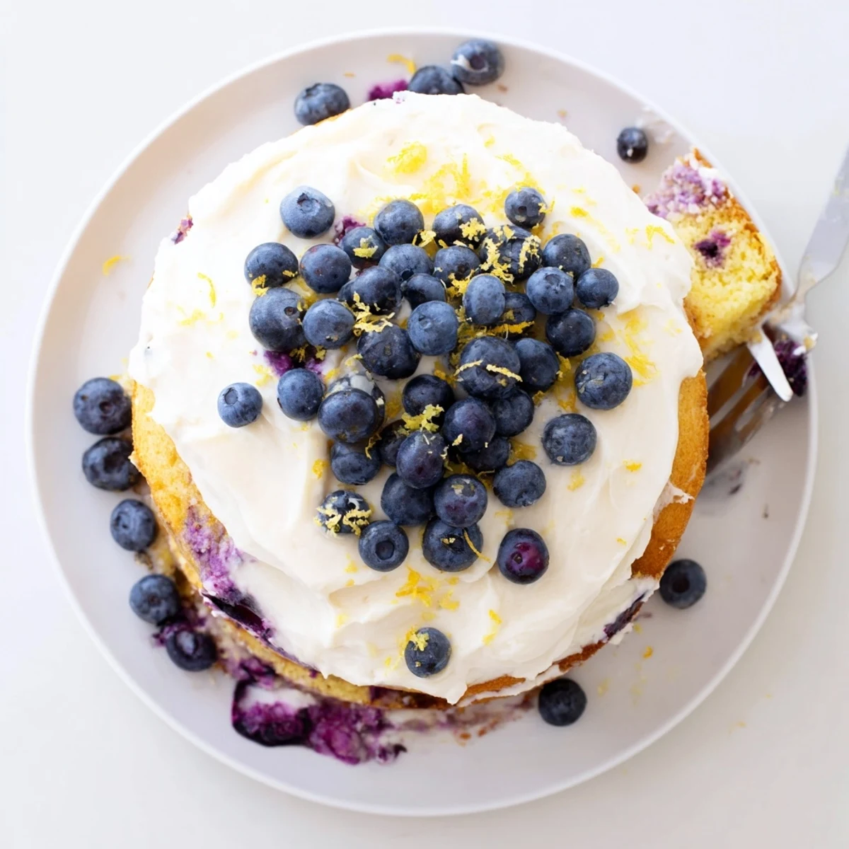 Freshly baked Lemon Blueberry Cake with Cream Cheese Frosting showcases juicy blueberries nestled in moist crumb.