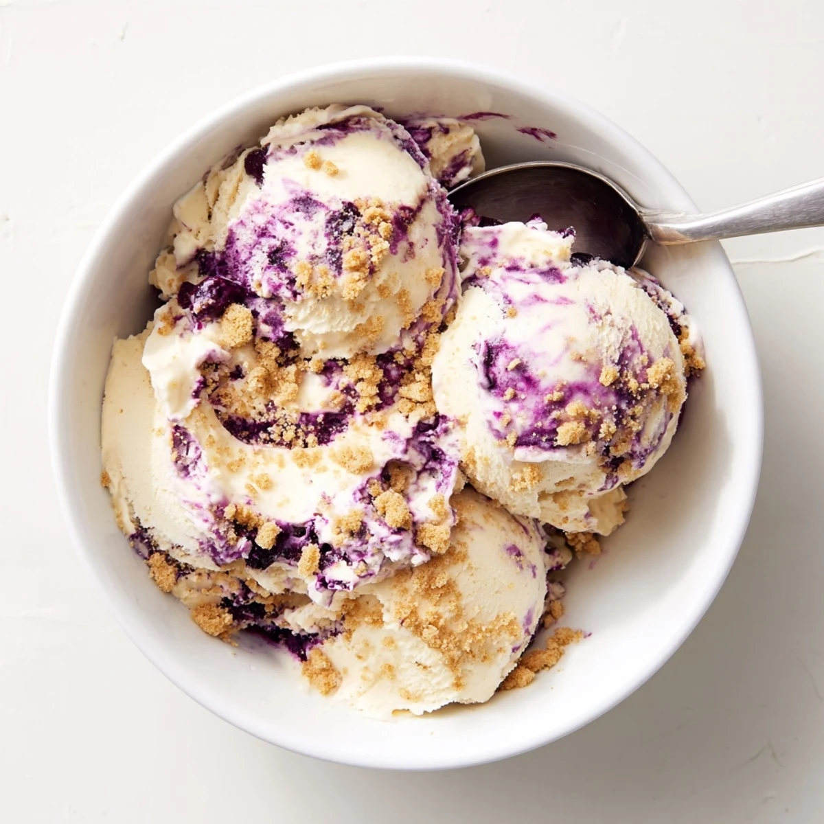 Lemon Blueberry Cheesecake Ice Cream frozen in a loaf pan, featuring vibrant purple berry ribbons and a golden graham topping for summer desserts.