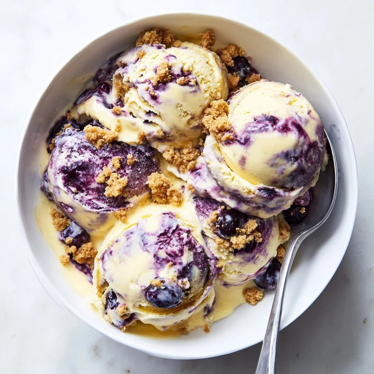 Close-up of Lemon Blueberry Cheesecake Ice Cream served on a chilled plate, highlighting tangy lemon zest flecks and plump blueberries in every bite.