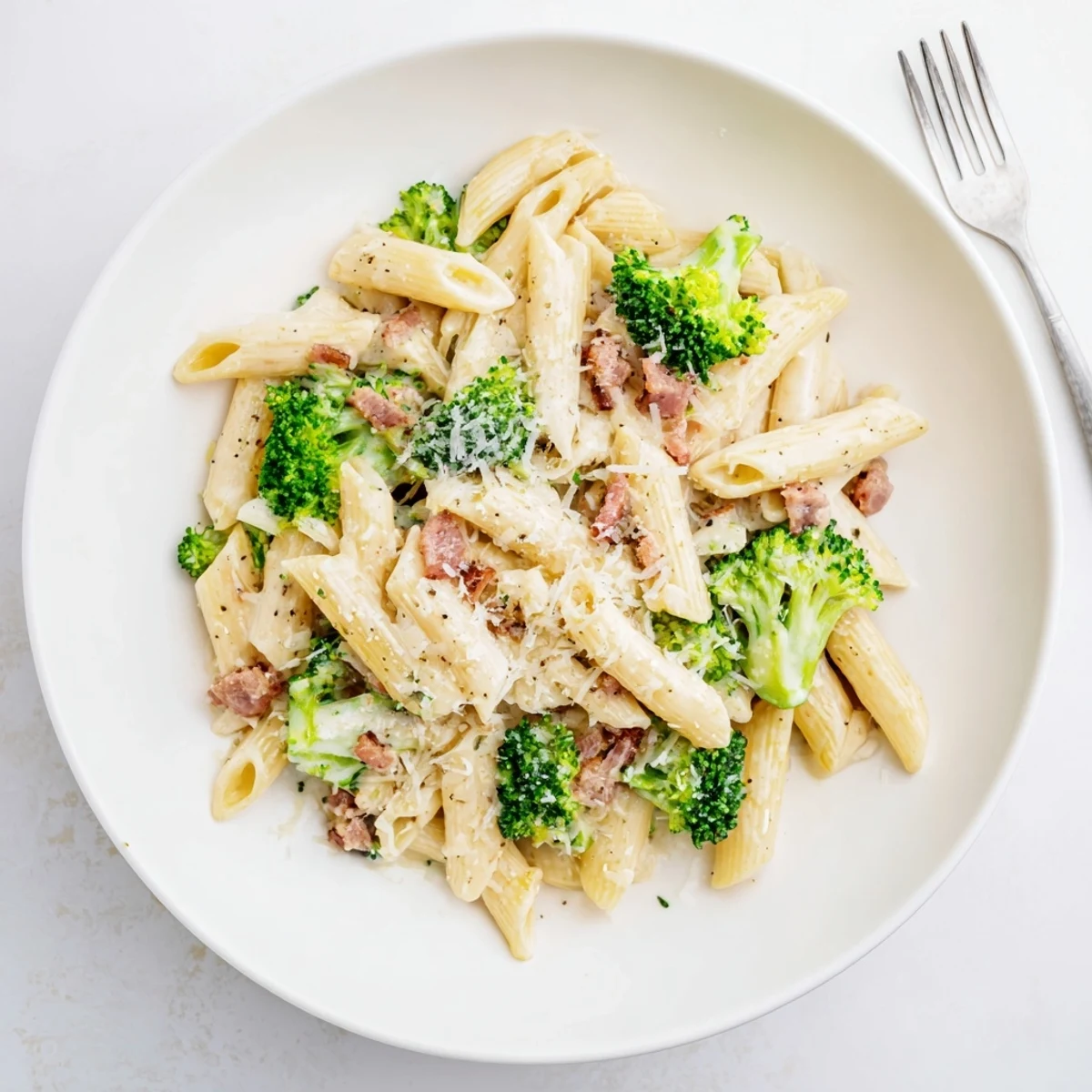 Close view of a fork lifting a bite of Bacon Broccoli and Parmesan Pasta, revealing the silky cream coating each noodle.