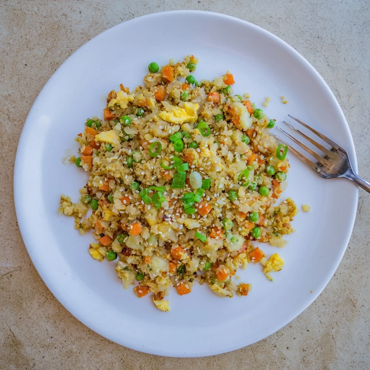 A close-up view of a colorful bowl of Cauliflower Fried Rice with Kimchi and Eggs, garnished with green onions and sesame seeds.