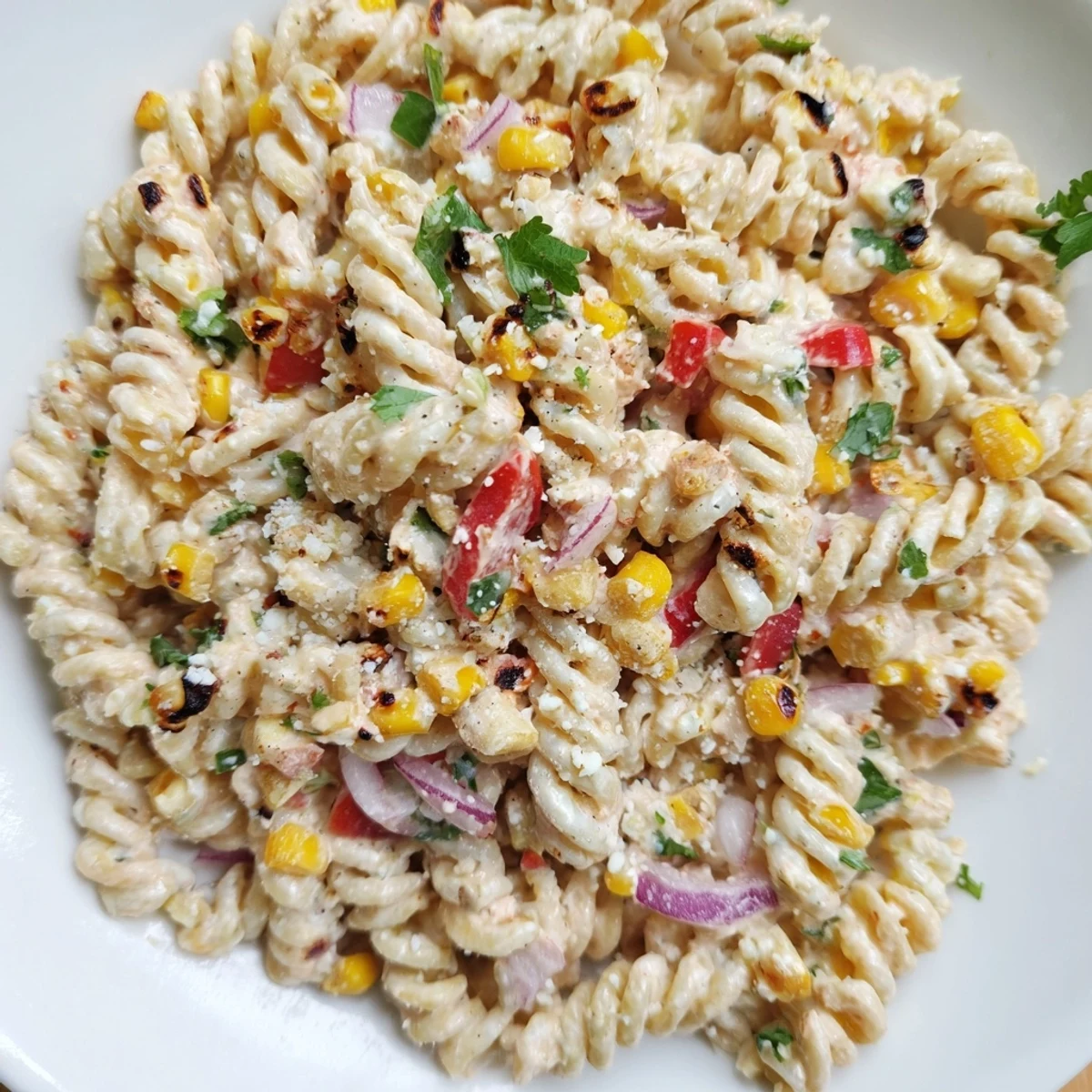 Spoonful of Mexican street corn pasta salad topped with fresh cilantro and chili powder against a dark background