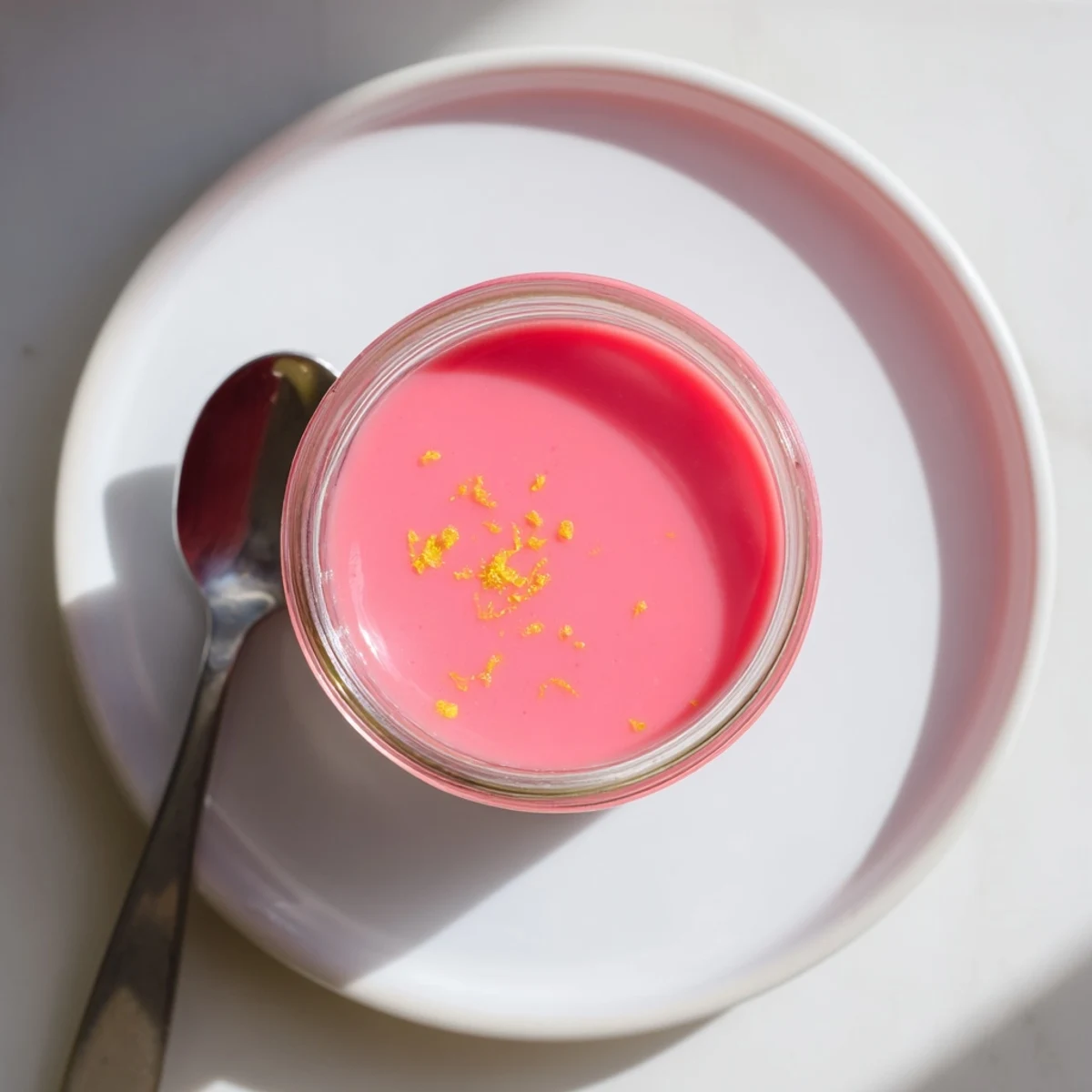 Silky homemade pink lemon curd in a glass jar with a small silver spoon