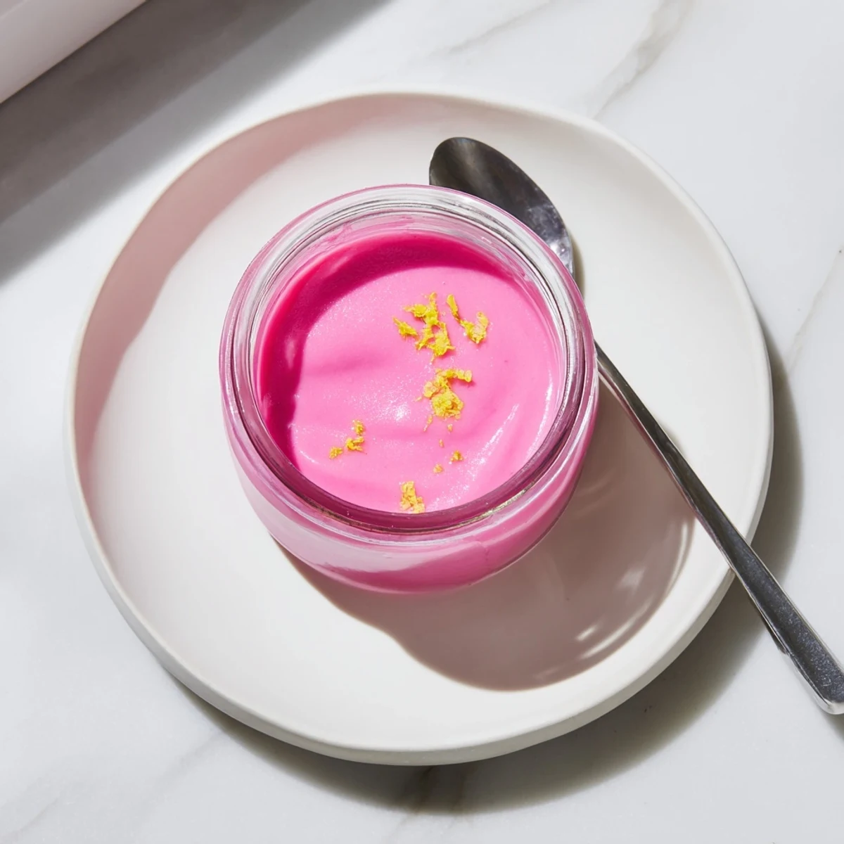 Vibrant pink lemon curd filling layered between two vanilla cake slices on a white plate