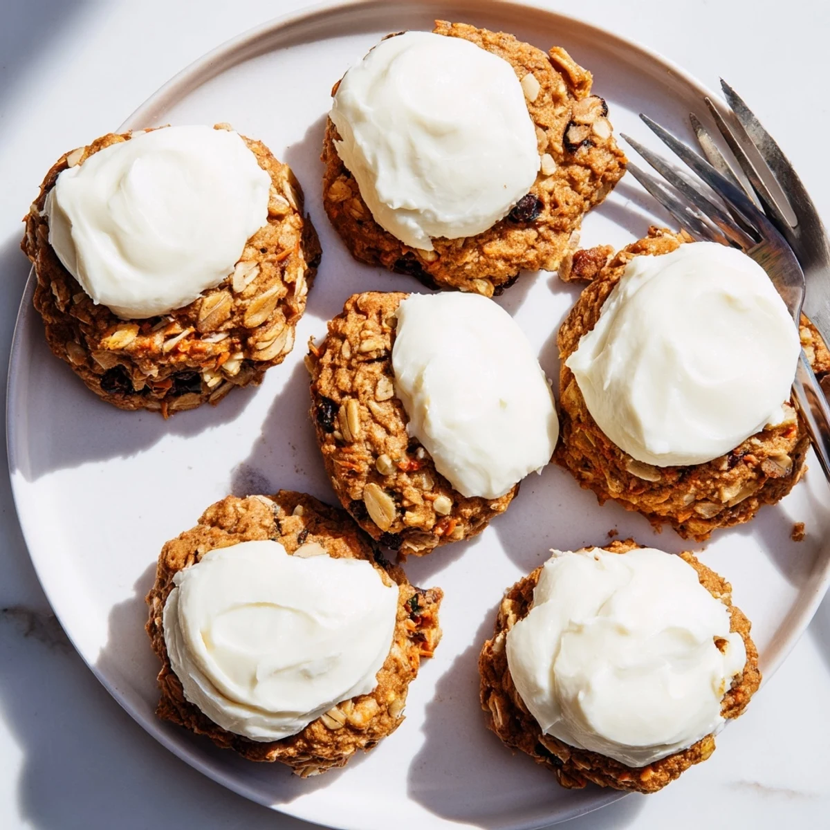 Soft carrot cake cookies topped with creamy cream cheese frosting on a white plate