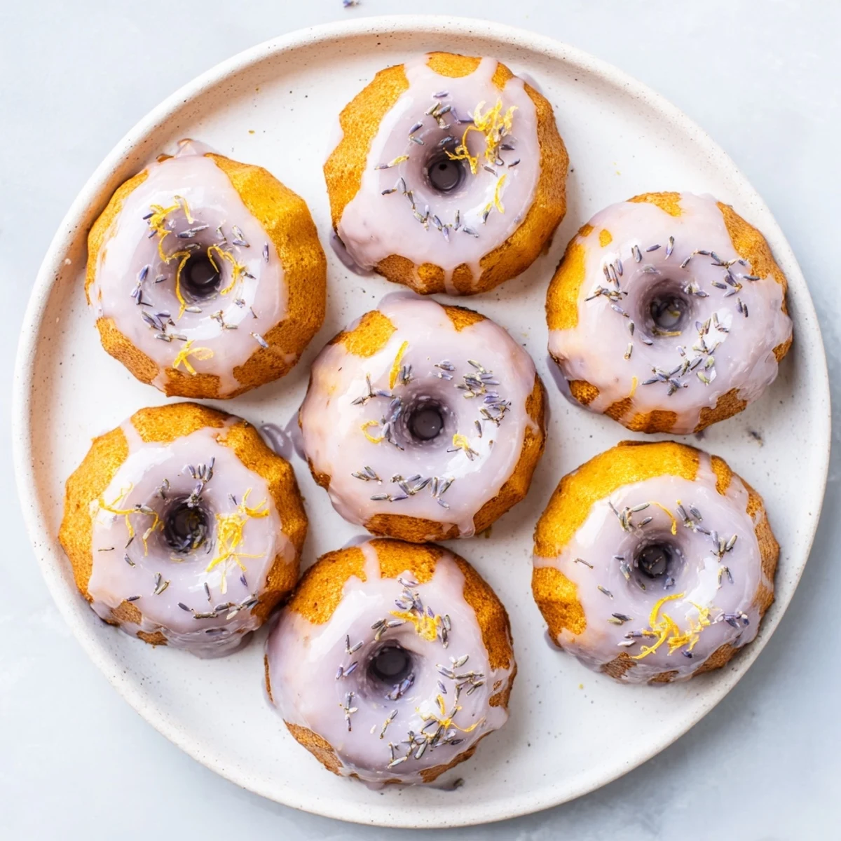 Golden mini lemon cakes with lavender glaze drizzled over freshly baked treats