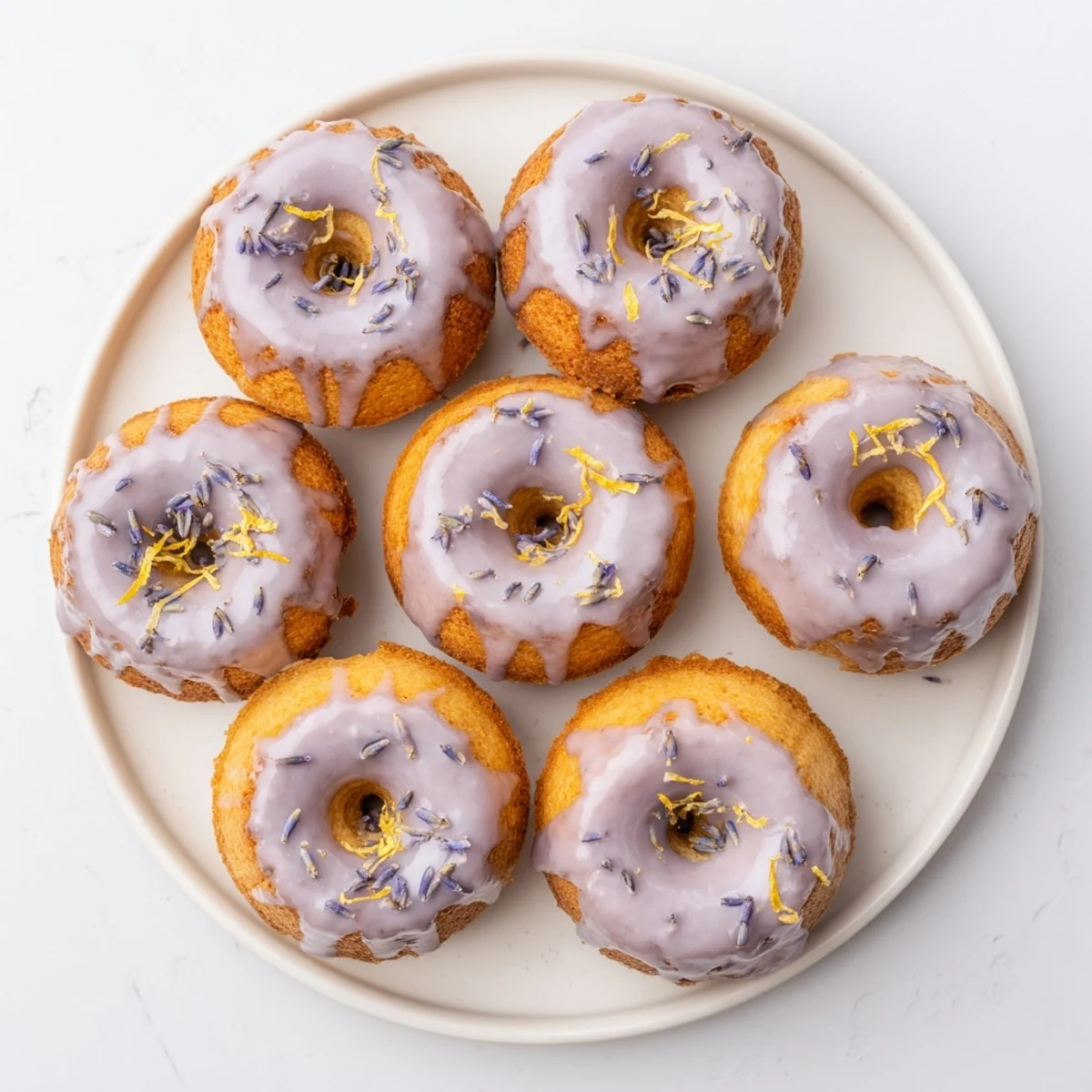 Small lemon cakes glazed with purple lavender frosting on a white serving plate