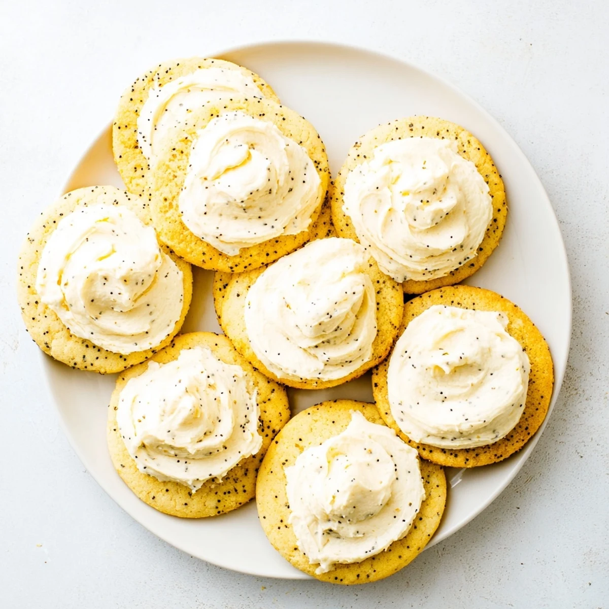 Lemon poppy seed cookies with white cheesecake frosting on white baking sheet