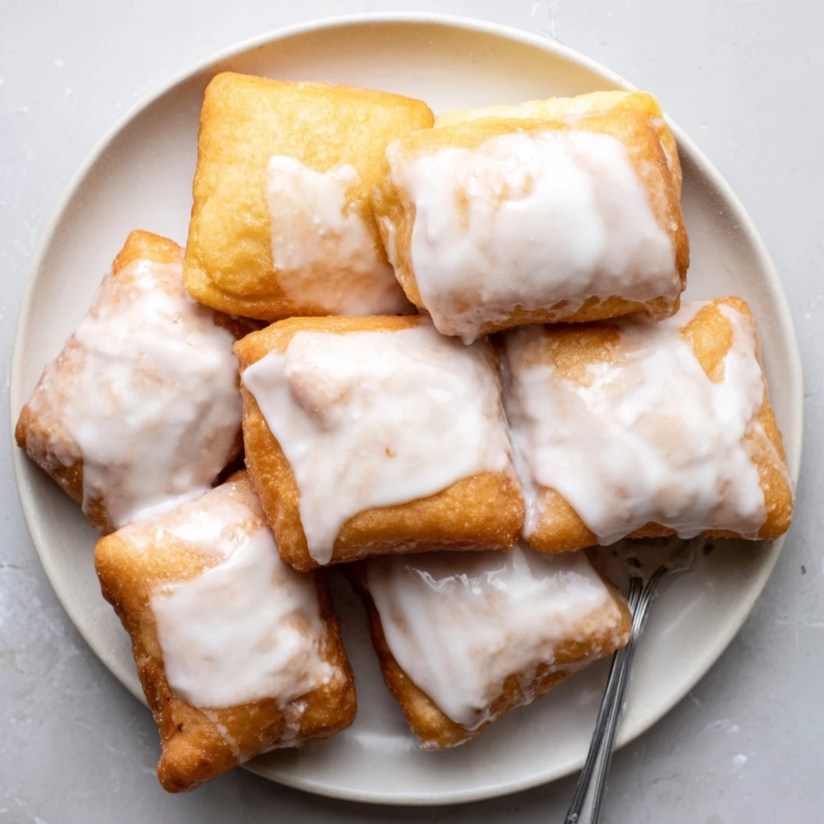 Golden glazed buttermilk beignet squares dusted with powdered sugar on a white plate