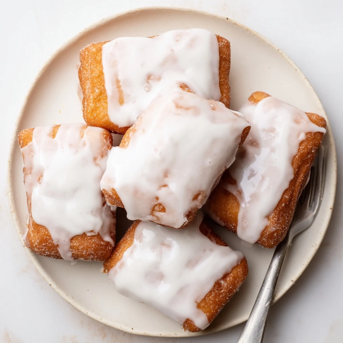 Fluffy fried beignet squares drizzled with sweet vanilla glaze and piled high