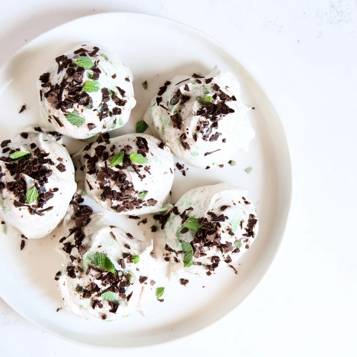 Dark chocolate and mint chip clouds featuring fluffy meringue cookies studded with chocolate and mint chips on a white baking sheet
