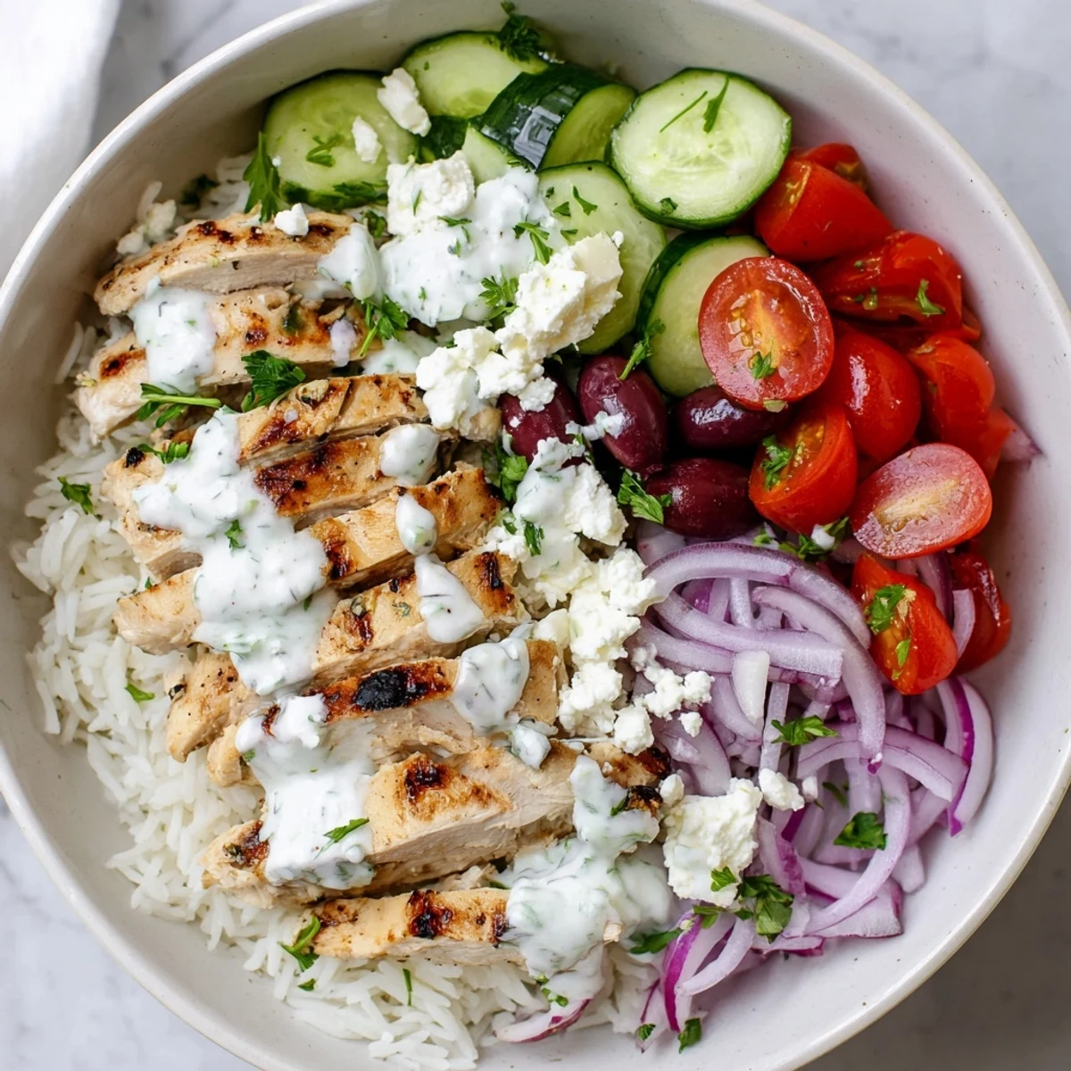 Sliced grilled chicken atop Greek chicken bowls with fresh cucumbers tomatoes olives and crumbled feta cheese garnish