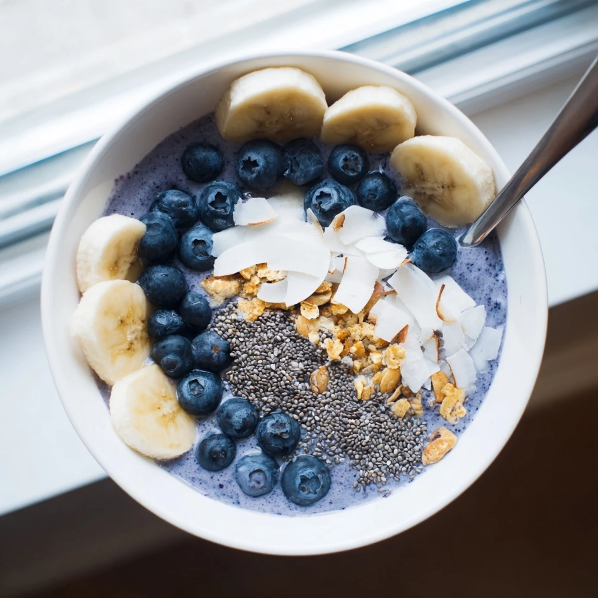 Creamy blueberry smoothie bowl with Greek yogurt topped with fresh berries, granola, and coconut flakes