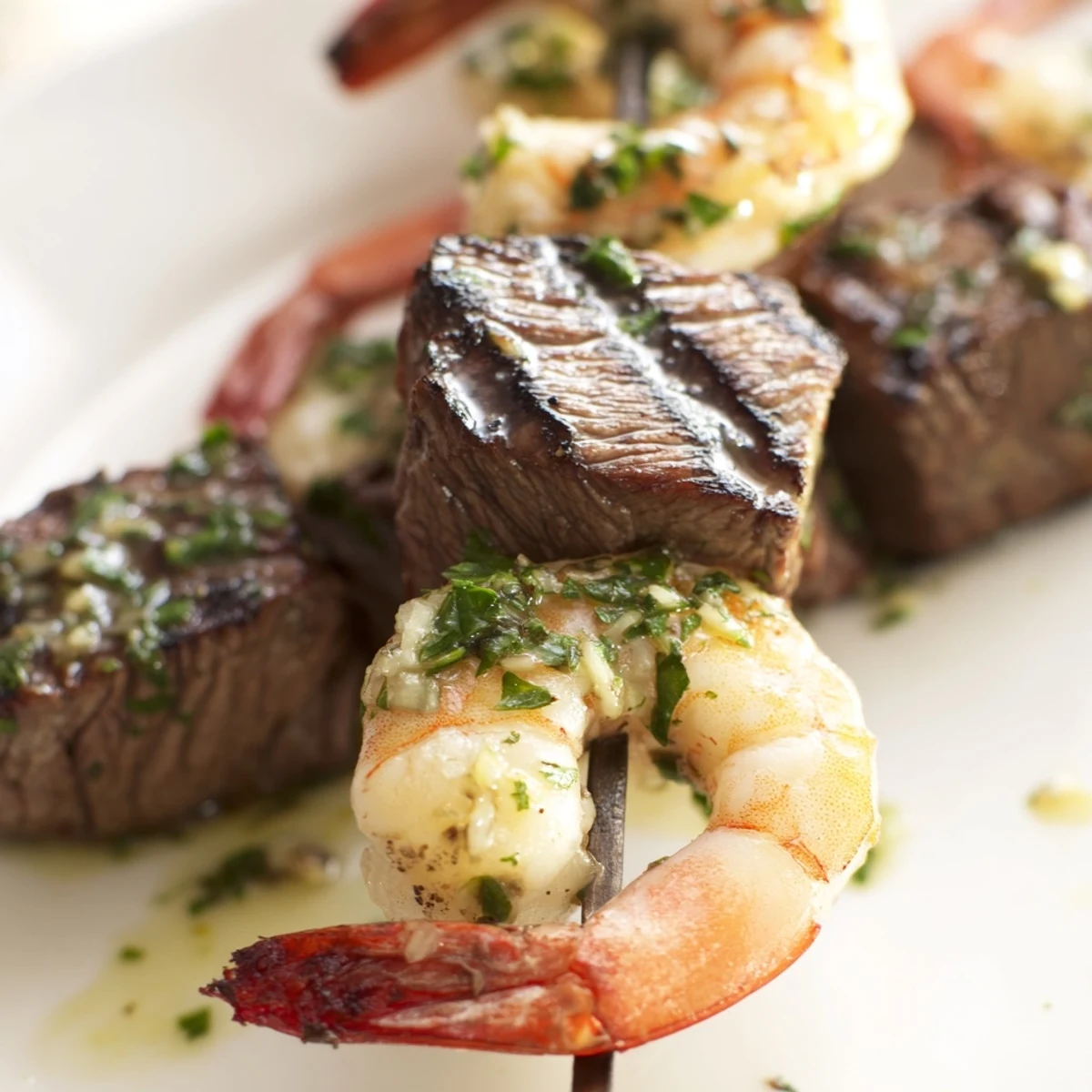 Golden grilled steak and shrimp skewers plated with lemon wedges and rich garlic butter glaze