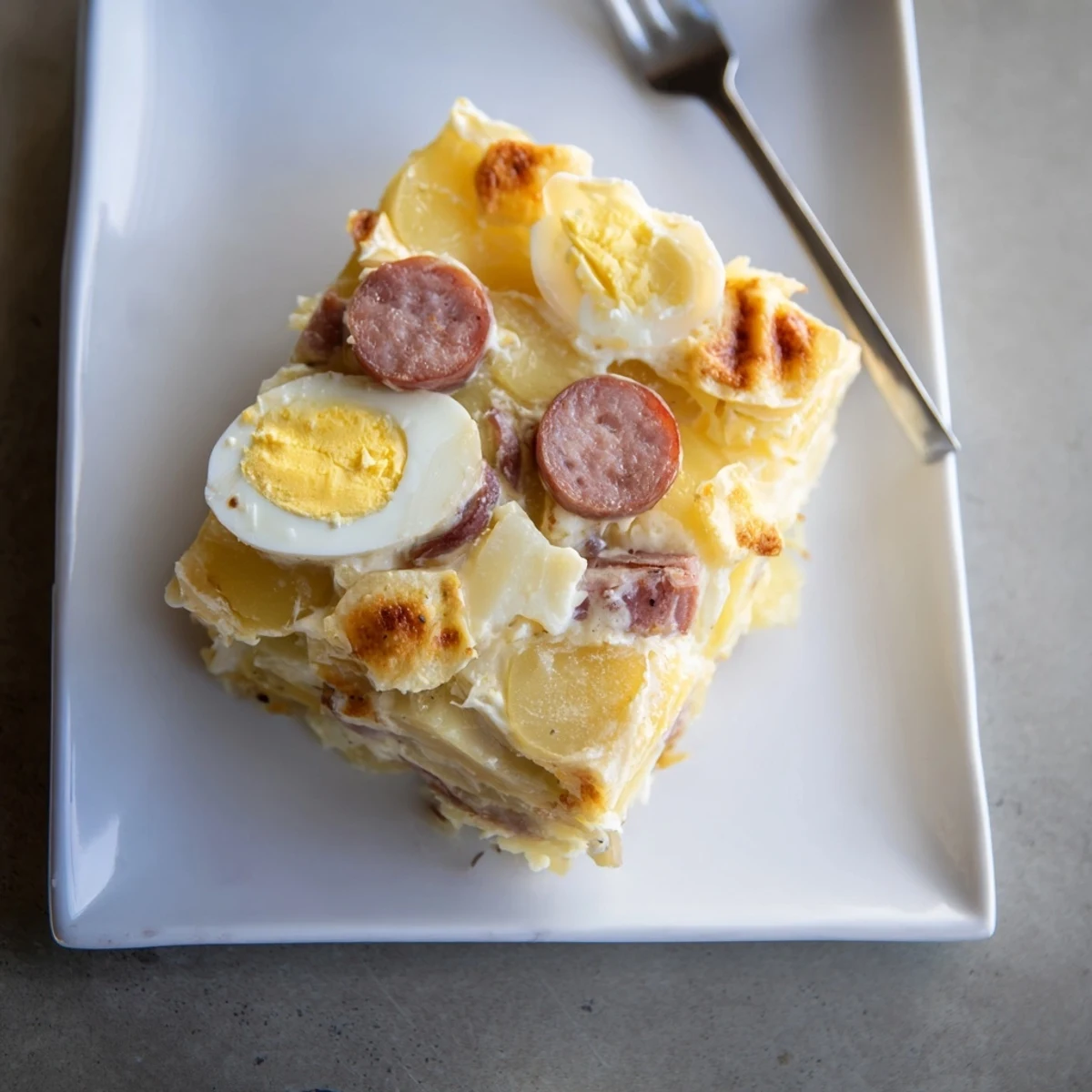 Comforting Hungarian potato casserole featuring sliced hard-boiled eggs, smoked sausage, and rich cream sauce