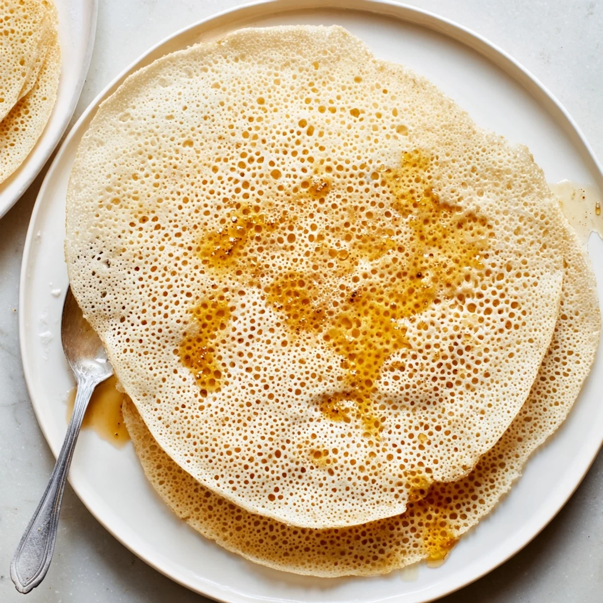 Close-up shot of Baghrir pancakes showing distinctive holey texture soaked in sweet honey butter glaze