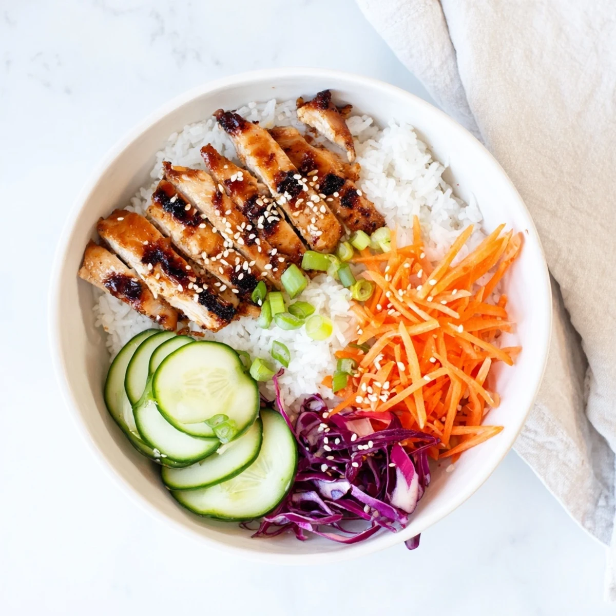 Heaping bowl of Korean BBQ chicken with colorful vegetable medley including purple cabbage, carrots, and cucumber over steamed white rice