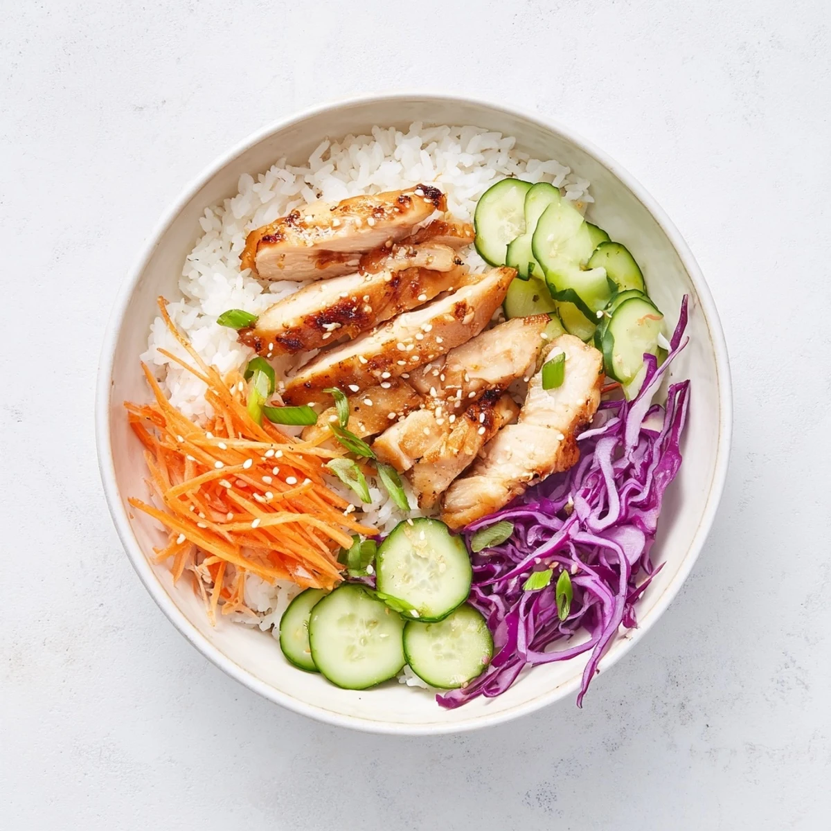 Sliced char-grilled Korean BBQ chicken arranged over jasmine rice with shredded carrots, sesame seeds, and fresh green onion garnish