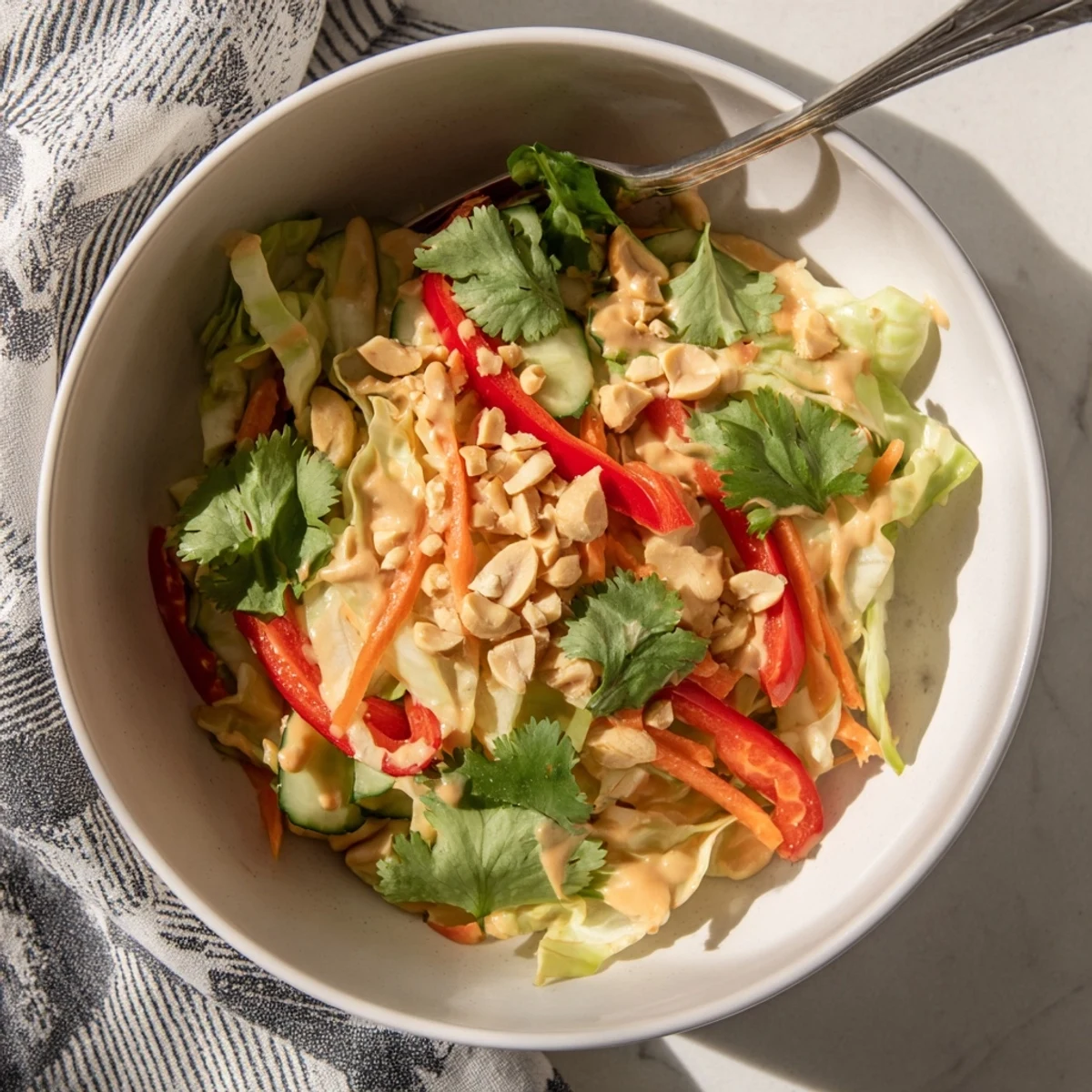 Vibrant vegetable salad topped with silky Thai peanut sauce garnished with roasted peanuts and fresh cilantro