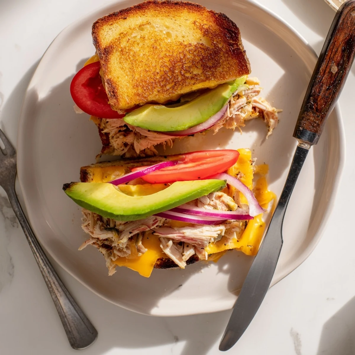 Sliced chicken avocado melt featuring creamy avocado and melted cheddar on rustic bread