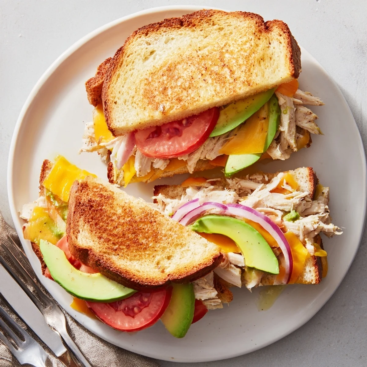 Warm grilled chicken avocado melt sandwich cut diagonally showing cheese and tomato layers