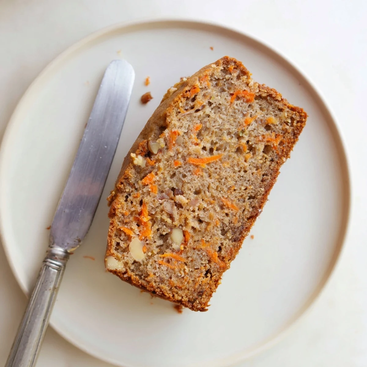 Golden carrot cake banana bread loaf topped with chopped walnuts and cinnamon spice on a white plate