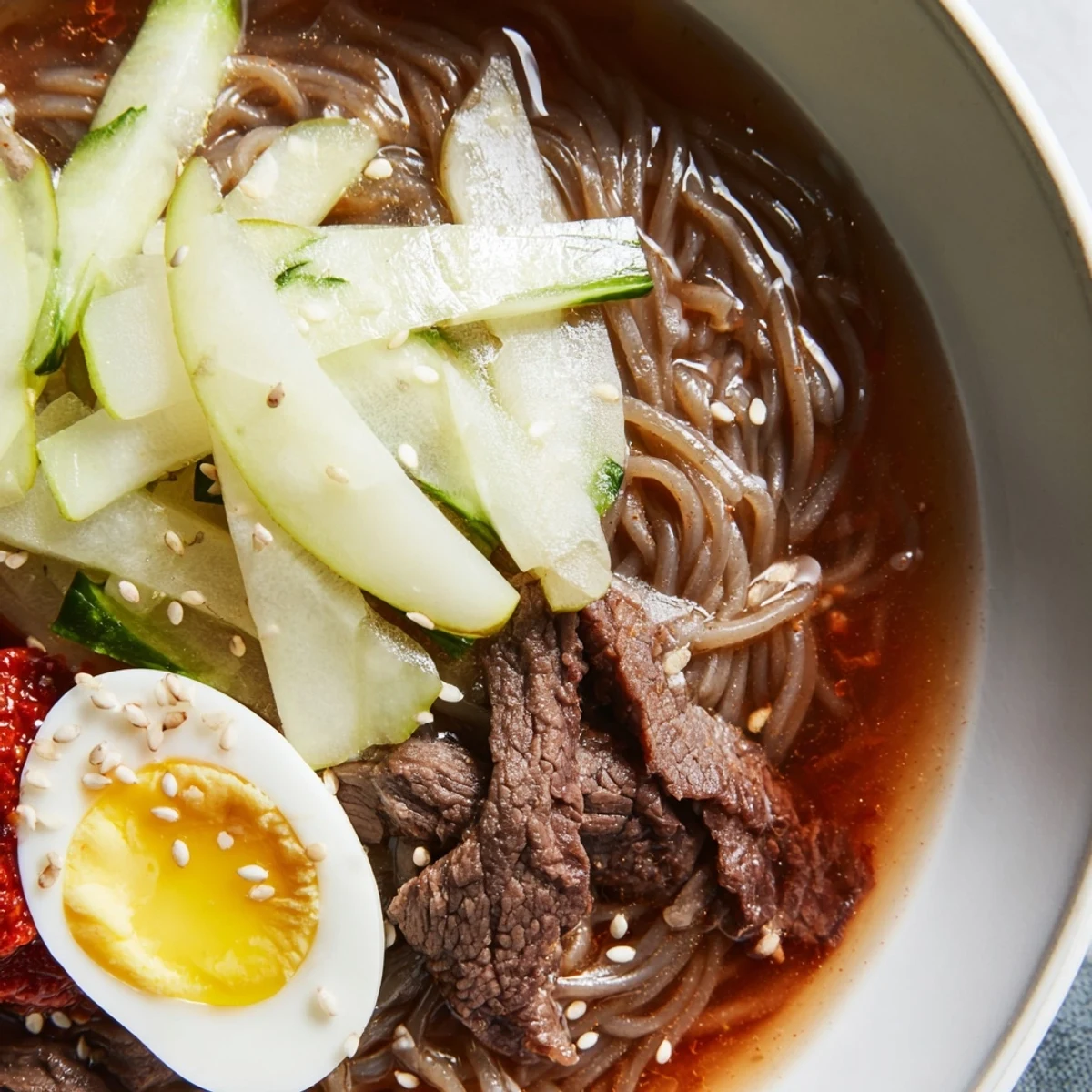 Chewy Korean naengmyeon noodles in icy tangy broth topped with sliced beef and egg