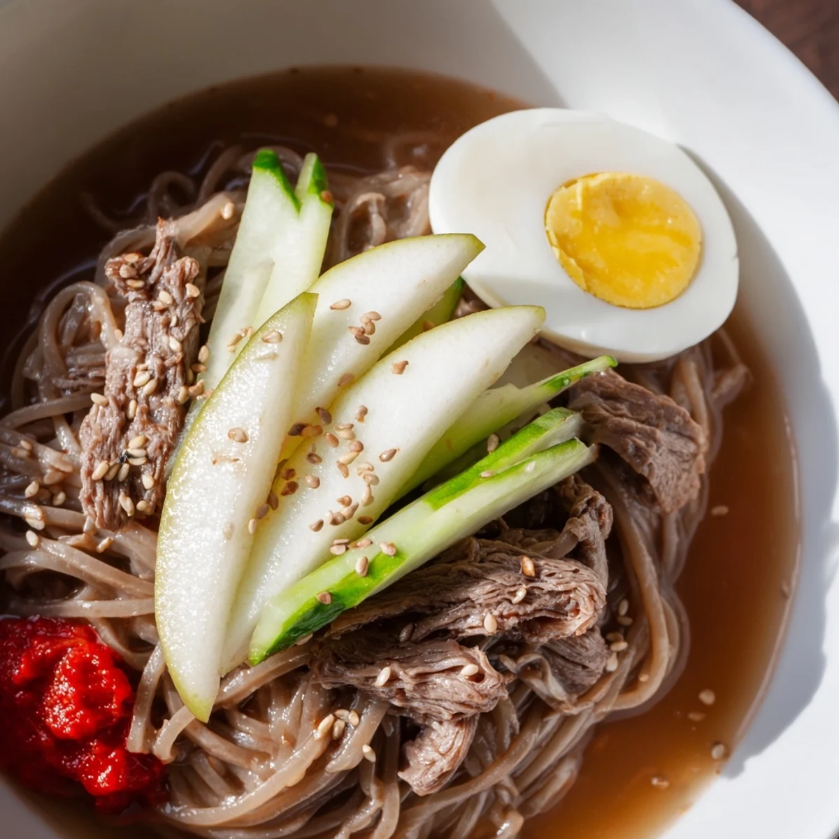 Cold Korean naengmyeon soup with buckwheat noodles cucumber pear and sesame garnish