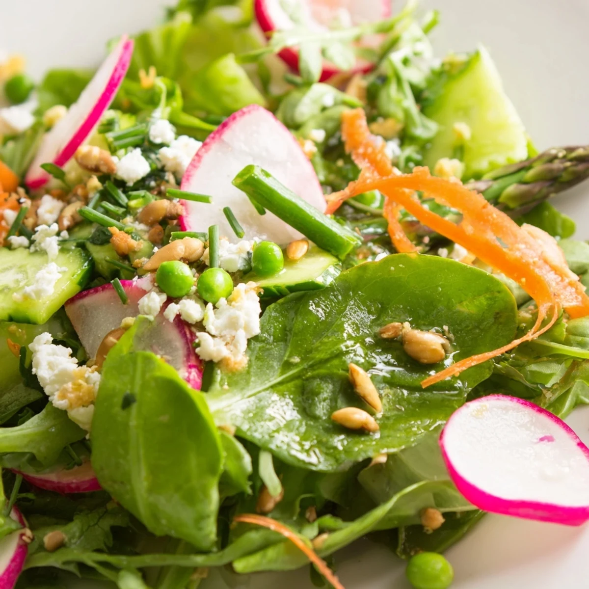 Fresh bright spring salad featuring tender greens, sweet peas, and creamy feta in a wooden bowl