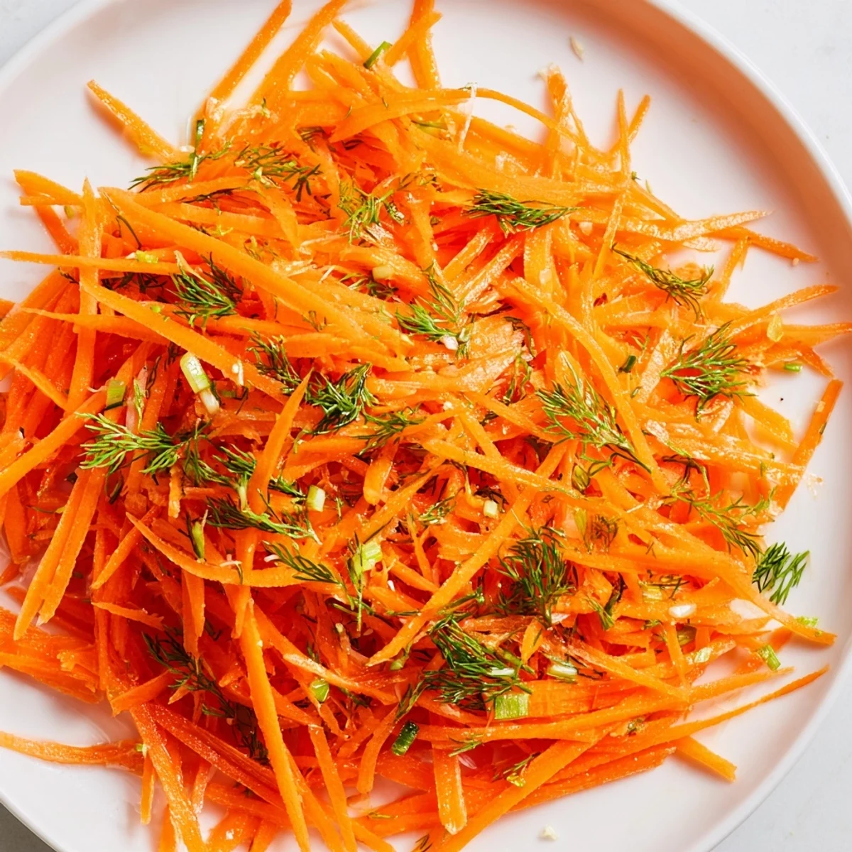 Crisp julienned carrots glistening with lemon dill dressing in a rustic ceramic dish