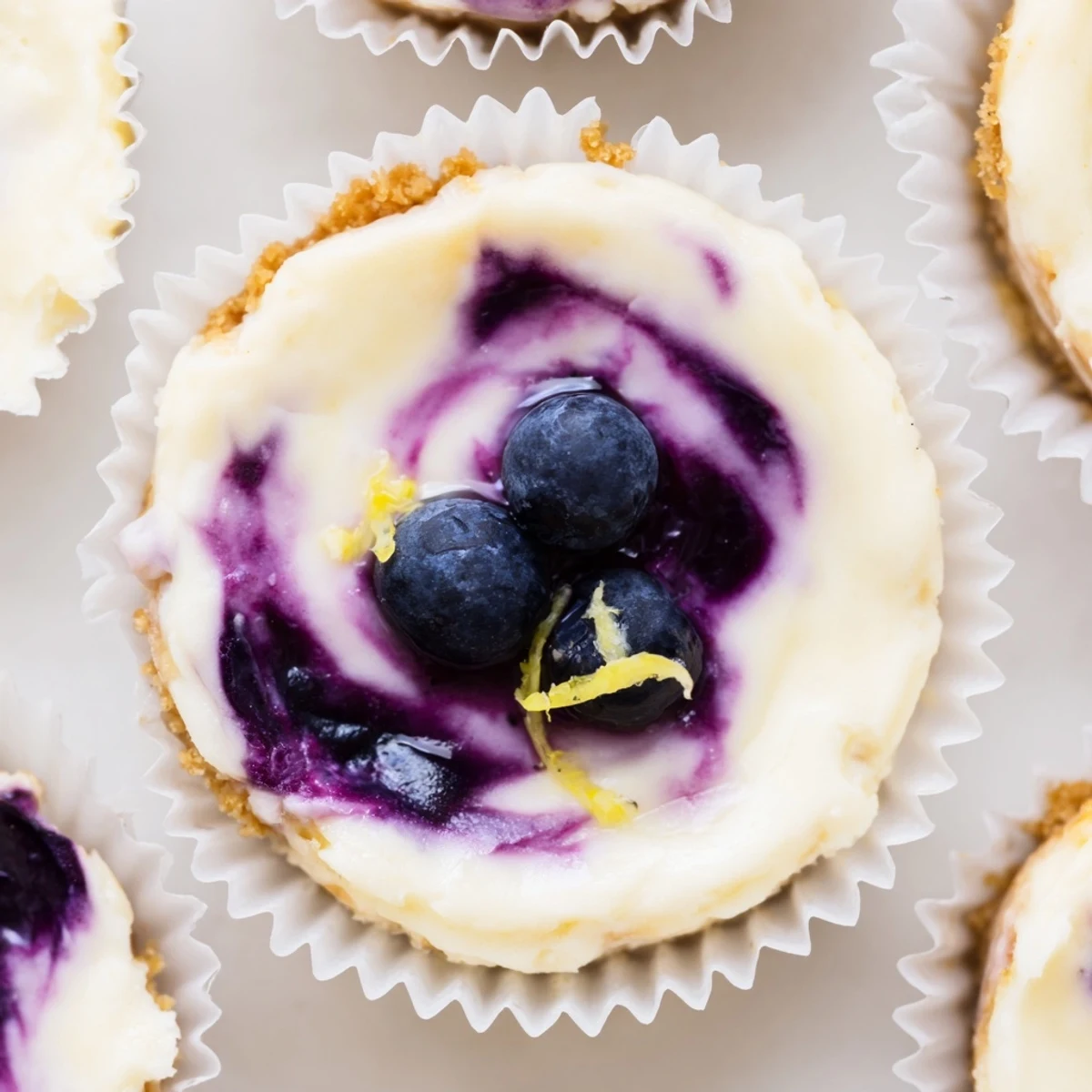 Mini lemon blueberry cheesecakes swirled with vibrant purple compote on a dessert plate