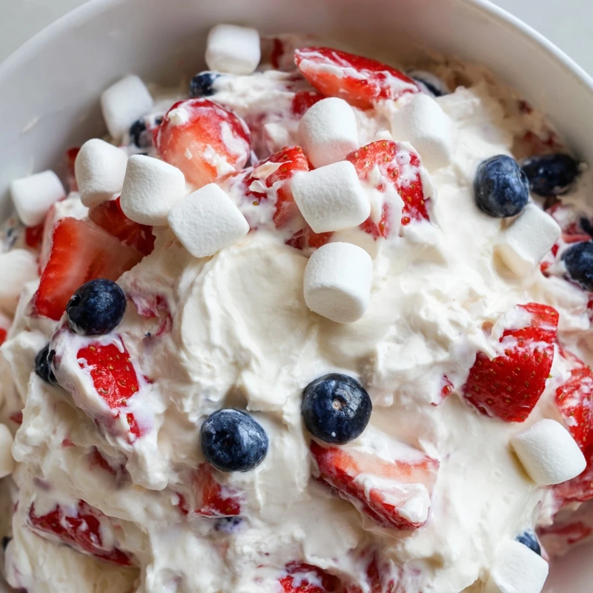 Vibrant red white blue cheesecake salad studded with marshmallows and ripe summer berries