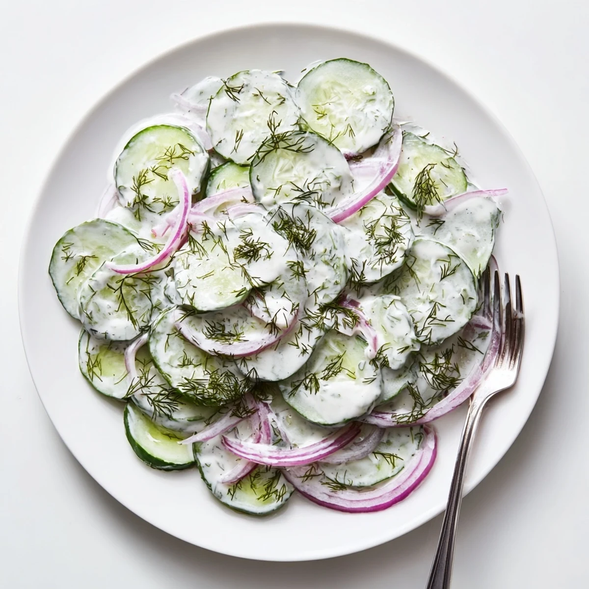 Fresh cucumber dill salad with thinly sliced vegetables in creamy white dressing served in glass bowl