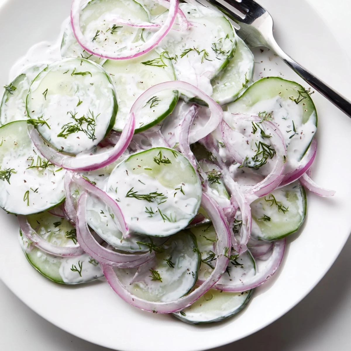 Crisp cucumber dill salad featuring red onions and herbs coated in tangy sour cream dressing