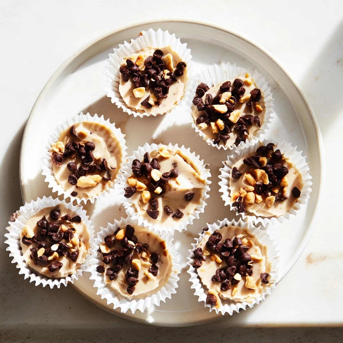 Frozen Peanut Butter Greek Yogurt Bites arranged in a mini muffin tin with chocolate chip toppings