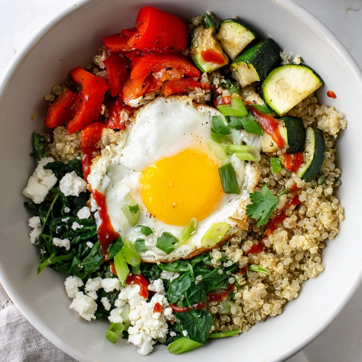 Steaming savory quinoa breakfast bowl garnished with fresh herbs and a drizzle of spicy sriracha