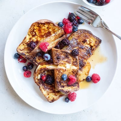 Golden-brown Crème Brûlée French Toast pieces rest on a white plate, drizzled with warm caramel sauce and fresh berries.