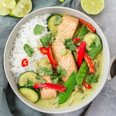 A vibrant green Thai curry salmon bowl served over jasmine rice with fresh lime wedges.