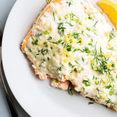 Herb-crusted Boursin salmon garnished with chives on a rustic parchment-lined baking sheet